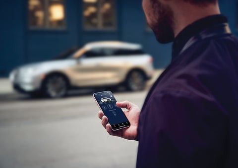 A person is shown interacting with a smartphone to connect to a Lincoln vehicle across the street. | Eby Lincoln in Goshen IN