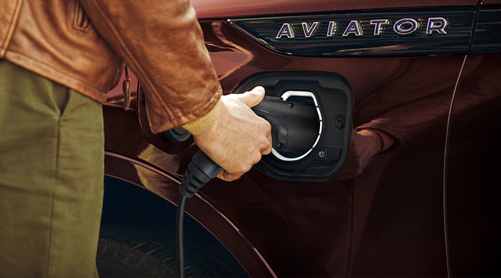 A hand is shown plugging a charger into the charging port of a 2023 Lincoln Aviator® Plug-in Hybrid model. | Eby Lincoln in Goshen IN